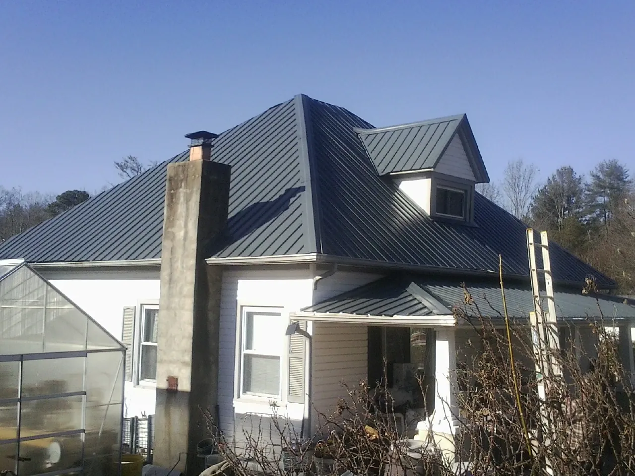 Dark blue standing seam metal roof on a white farmhouse with dormer — Slate & Tile Roof Repair by Roofing Brothers in Alum Bank