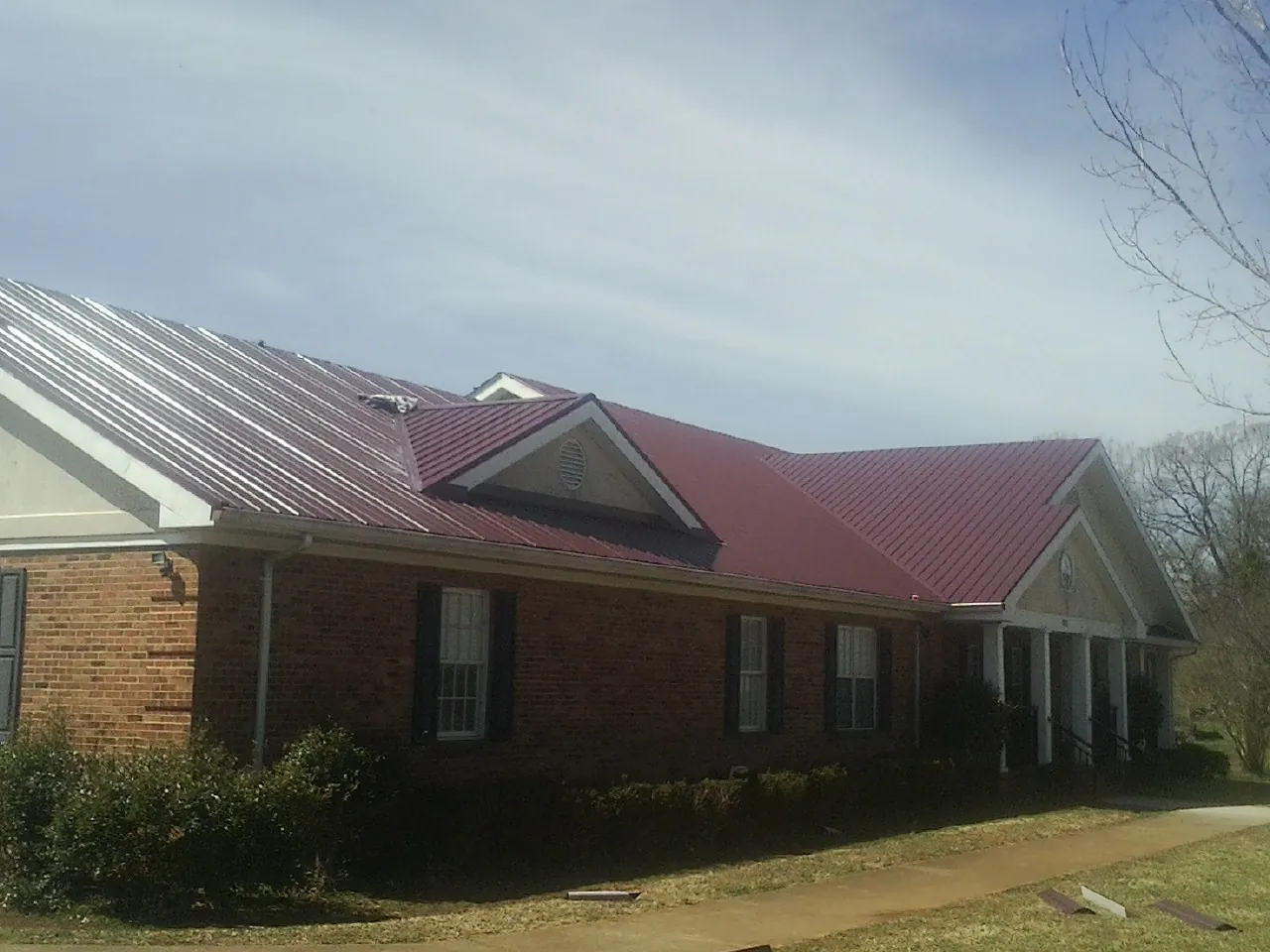 Red metal roof with gabled entries on a long brick building, from a Hail Damage Roof Repair job in Alum Bank