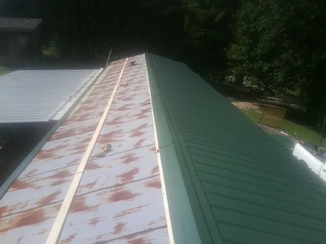 Old rusted panels beside newly installed green metal roofing — Wind Damage Roof Repair by Roofing Brothers in Alum Bank