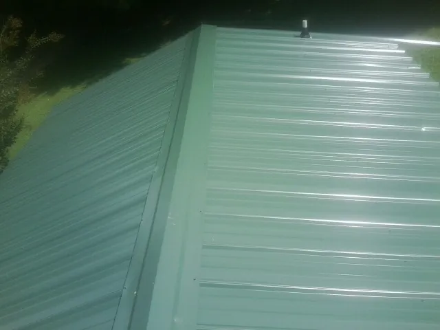 New green metal panels meeting at the ridge of a roof — Flat Roof Repair work by our crew in Alum Bank