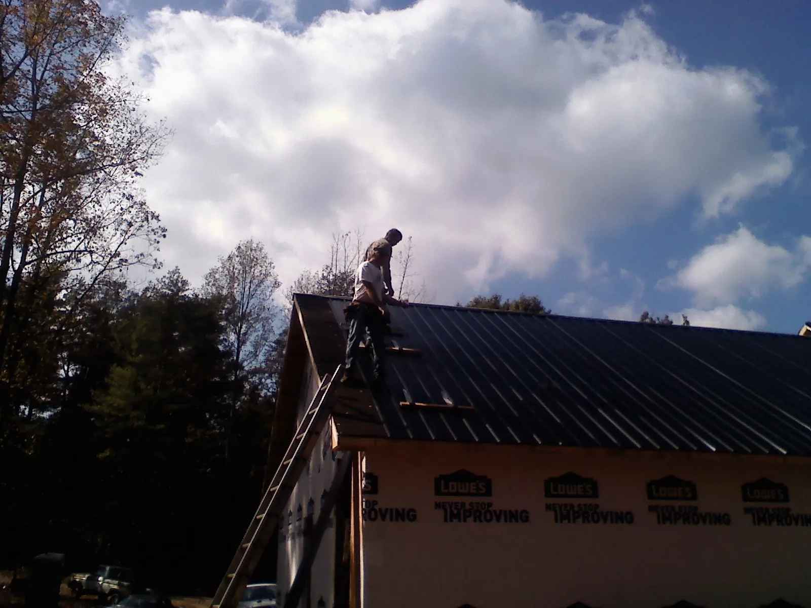 Roofer fastening dark metal panels high against a cloudy sky, from a Roof Inspection job in Alum Bank