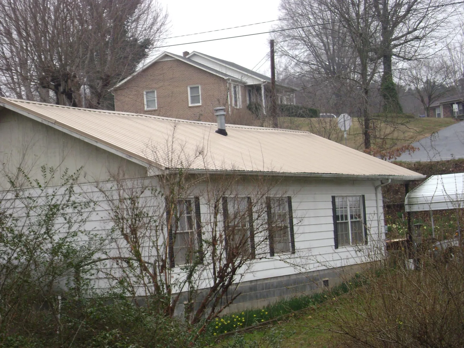 Tan metal roof on a white sided house set into a hillside — Commercial Roofing by Roofing Brothers in Alum Bank