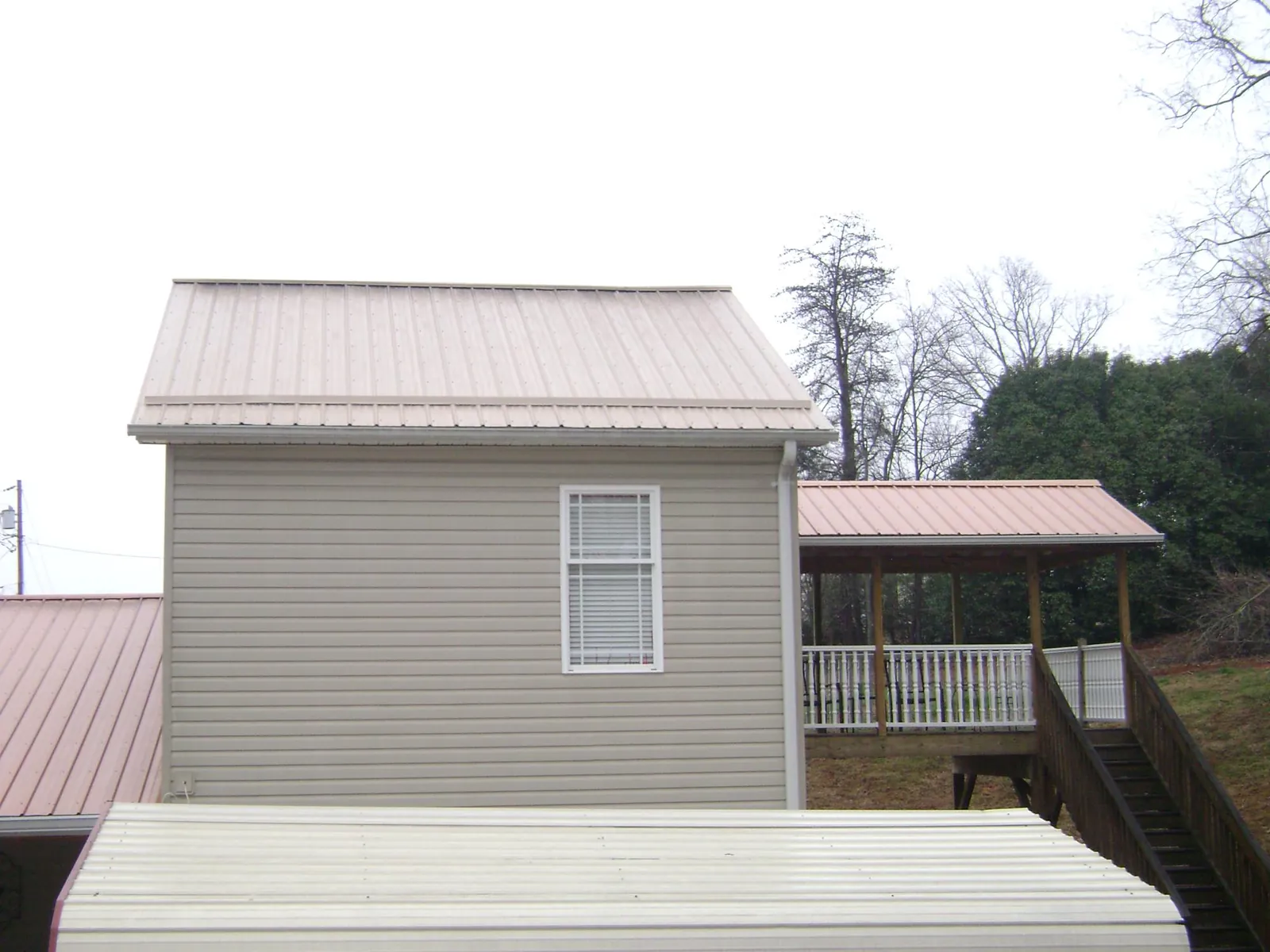Tan metal roofs on a two story addition and attached porch, from a Roof Replacement job in Alum Bank